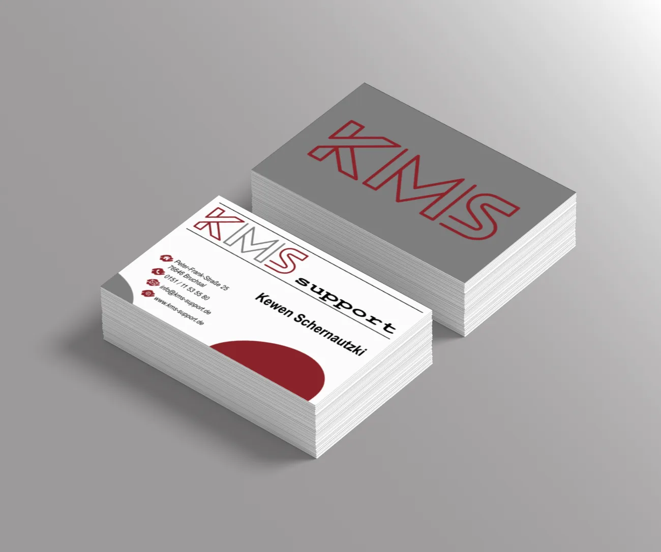 Zwei Stapel Visitenkarten von KMS-support: eine Seite weiß mit rotem Bogen, die andere grau mit großem KMS-Schriftzug